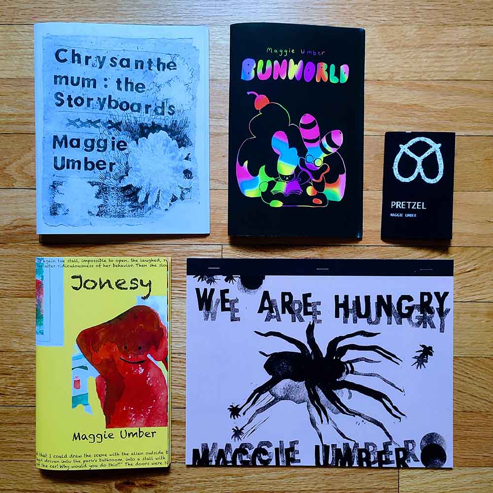books laying slanted on a wooden floor, with text that reads chrysanthemum: the Storyboards Maggie Umber, Maggie Umber Bunworld, PRETZEL Maggie Umber, Jonesy Maggie Umber, WE ARE HUNGRY MAGGIE UMBER