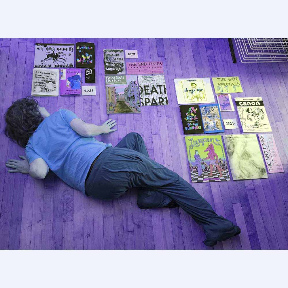 Maggie Umber holding her comic zine, text reads: MAC Fest, The GOK Specials, Maggie Umber